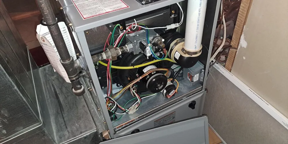 Une vue rapprochée de l'intérieur d'une fournaise au gaz résidentielle à haute efficacité avec le panneau avant retiré. On y voit le moteur de tirage, l'ensemble de la valve à gaz, ainsi que divers câblages électriques et capteurs.