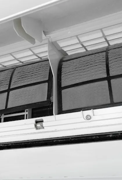 Un gros plan d'un climatiseur mural avec le panneau avant ouvert, révélant deux filtres à tamis lourdement obstrués par une épaisse poussière grise. Une main retire l'un des filtres.